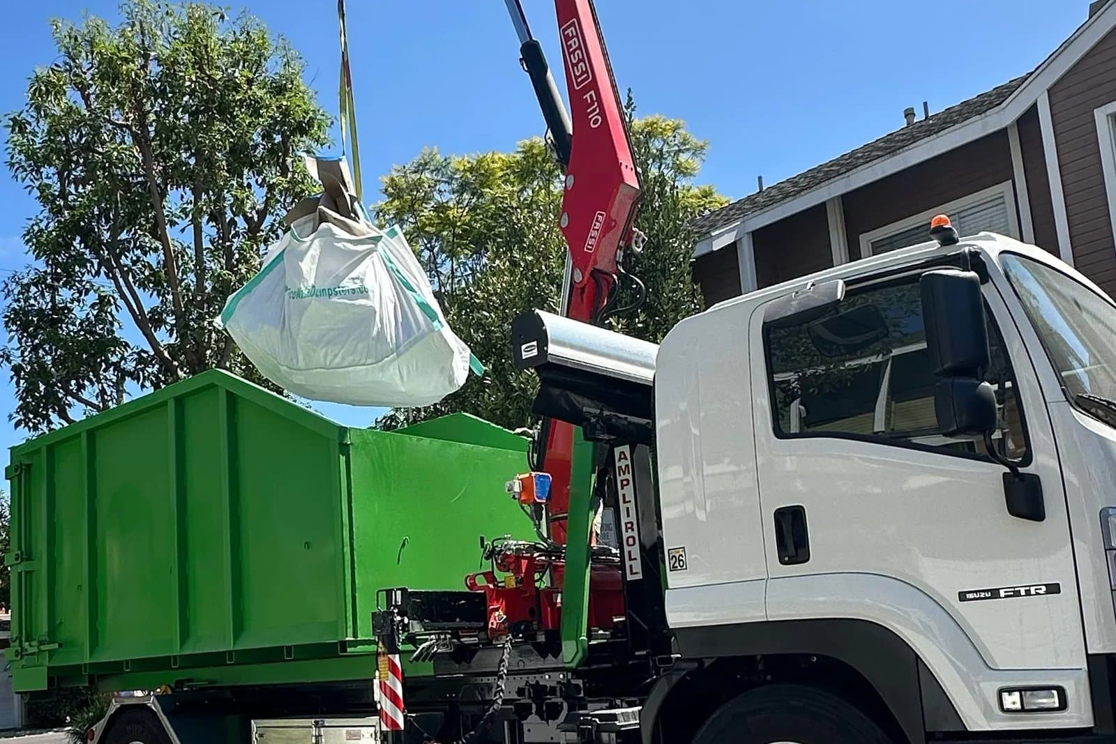 Eco Waste's crane truck lifting a full white dumpster bag off a residential street
