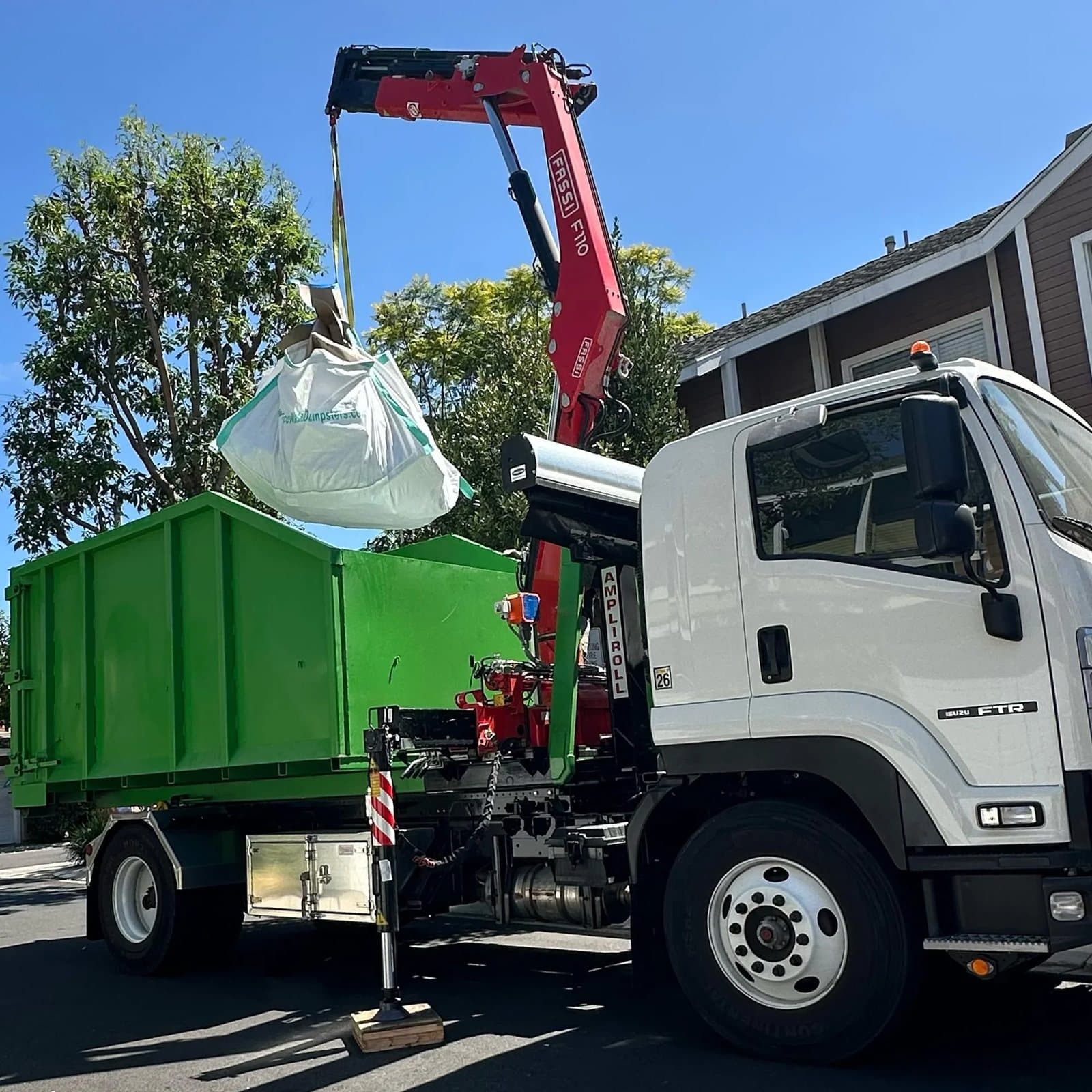 Eco Waste's crane truck lifting a full dumpster bag on a residential street