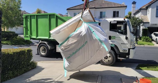 Full dumpster bag lifted by crane beside the Eco Waste truck