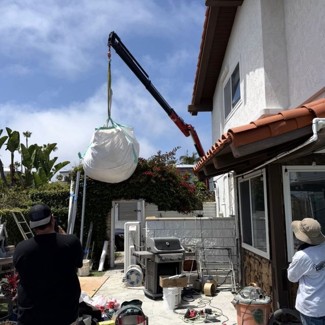 Crane lifting a full dumpster bag out of a backyard remodel